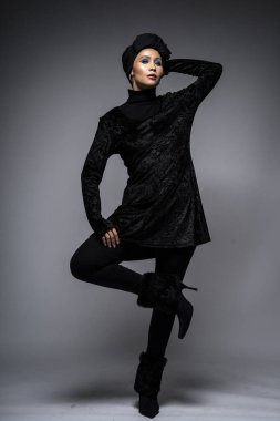 Siyah bluzlu ve gri arka planda türbanı olan Asyalı bir kadının yüksek moda portresi. Başörtüsü modası için moda editörlüğü konsepti. Tam uzunluk
