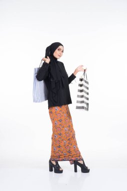 Güzel bir Asyalı kadın manken batik sarong ve tesettürlü siyah bir bluz giyiyor. Beyaz arka planda izole edilmiş. Eidul Fitri ya da bayram alışverişi. Tam boy portre