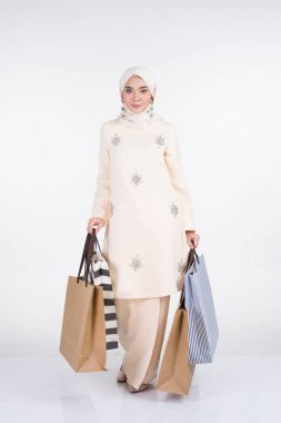 Kurung Pahang 'ın beyaz arka planda izole edilmiş alışveriş torbaları taşıyan geleneksel Asya elbisesi içinde güzel bir Müslüman kadın manken. Eidul Fitri festival hazırlık alışveriş konsepti. Tam boy portre.