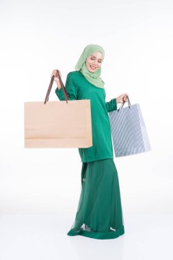 Modern bir kurungda beyaz arka planda izole edilmiş alışveriş torbaları taşıyan güzel bir Asyalı kadın model. Eidul Fitri festival hazırlık alışveriş konsepti. Tam boy portre.