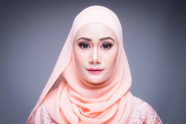 Headshot of a beautiful Muslim female model in an Asian Muslim traditional dress and hijab isolated on grey background. Eidul fitri fashion and lifestyle portrait concept