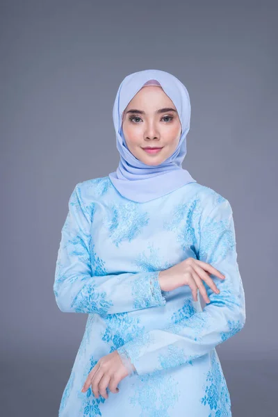 Beautiful Muslim female model wearing pastel blue modern kurung with hijab, a urban lifestyle apparel for Muslim women isolated on grey background. Beauty and hijab fashion concept. Half length