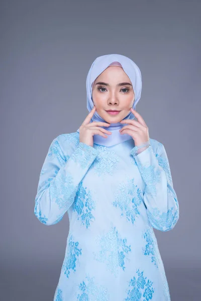 Beautiful Muslim female model wearing pastel blue modern kurung with hijab, a urban lifestyle apparel for Muslim women isolated on grey background. Beauty and hijab fashion concept. Half length