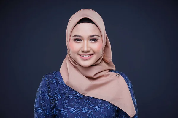 Closeup of a beautiful female Muslim model wearing dark blue modern kurung with hijab, a modern urban lifestyle apparel for Muslim women isolated on grey background. Beauty and hijab fashion concept.