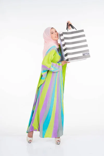 白を基調としたショッピングバッグを背景に 伝統的なカフタン カフタンのドレスを身に着けた美しく幸せなムスリム女性モデル Eidul Fitriファッションとお祝いの準備ショッピングコンセプト — ストック写真