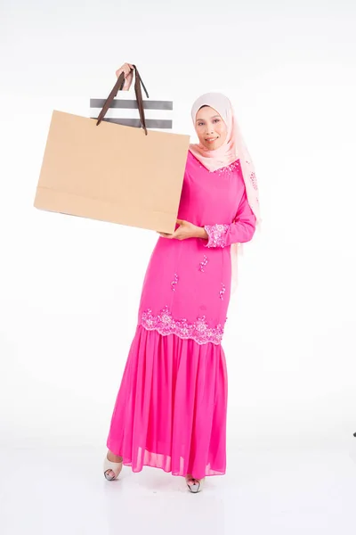 白を基調としたショッピングバッグを背景に伝統的なピンクのモダンなクルンで美しく興奮したイスラム教徒の女性モデル Eidul Fitriファッションとお祝いのショッピングコンセプト — ストック写真