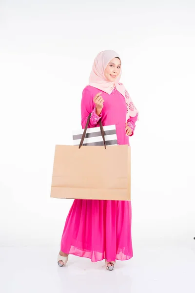 一位美丽而兴奋的穆斯林女模特 穿着传统的粉色现代和服 背着白色背景的购物袋 Eidul Fitri时尚和节庆购物理念 — 图库照片