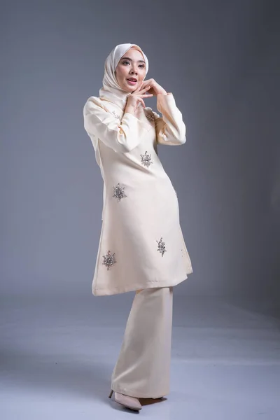 Beautiful female Muslim model wearing kurung Pahang and hijab, an urban lifestyle apparel for Muslim women on grey. Beauty and hijab fashion concept. Full length portrait