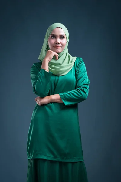 Half length portrait of a beautiful female Muslim model in modern kurung and hijab, an urban lifestyle apparel for Muslim women on green background. Beauty and hijab fashion portrait concept.