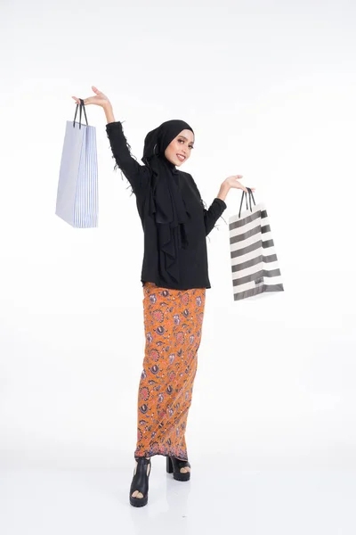 美しい女性アジアのモデルは バティックサロンとヒジャーブの紙袋を保持して黒の上を身に着けています 白地に隔離されてる Eidul FitriまたはEidショッピングコンセプト 全長像 — ストック写真