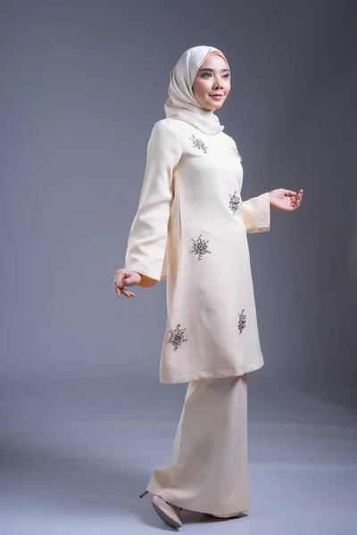 Beautiful female Muslim model wearing kurung Pahang and hijab, an urban lifestyle apparel for Muslim women on grey. Beauty and hijab fashion concept. Full length portrait