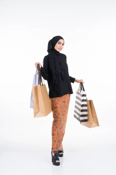 漂亮的亚洲女模特 身穿黑色上衣 头戴蜡染沙龙 头戴头巾 手持纸袋 被白色背景隔离 Eidul Fitri或Eid Shopping概念 全长肖像 — 图库照片