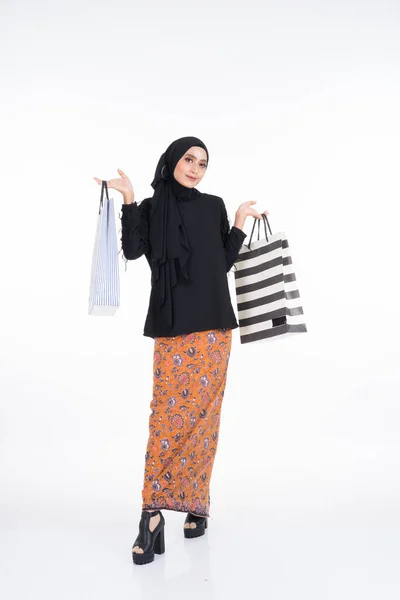 美しい女性アジアのモデルは バティックサロンとヒジャーブの紙袋を保持して黒の上を身に着けています 白地に隔離されてる Eidul FitriまたはEidショッピングコンセプト 全長像 — ストック写真