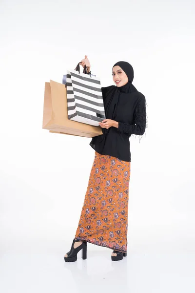 漂亮的亚洲女模特 身穿黑色上衣 头戴蜡染沙龙 头戴头巾 手持纸袋 被白色背景隔离 Eidul Fitri或Eid Shopping概念 全长肖像 — 图库照片