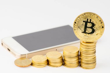 Fintech, iş ve kripto para birimi konsepti. Akıllı telefonlu bir yığın altın para ve beyaz arka planda Bitcoin.