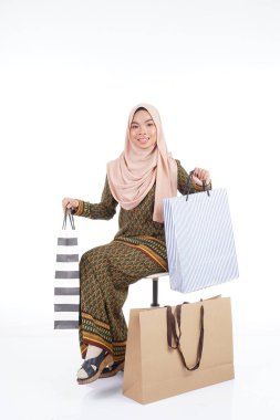 Geleneksel Asya elbisesi içinde güzel bir Müslüman bayan üniversite öğrencisi beyaz arka planda izole edilmiş alışveriş torbaları taşıyan modern kurung. Eidul Fitri moda ve festival alışveriş konsepti.