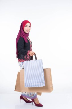 Beyaz arka planda izole edilmiş alışveriş torbaları taşıyan, Asyalı geleneksel elbiseli güzel bir Müslüman kadın manken. Idul fitri festival hazırlık alışveriş konsepti. Tam boy portre.