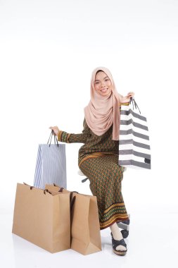 Geleneksel Asya elbisesi içinde güzel bir Müslüman bayan üniversite öğrencisi beyaz arka planda izole edilmiş alışveriş torbaları taşıyan modern kurung. Eidul Fitri moda ve festival alışveriş konsepti.