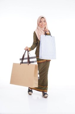 Geleneksel Asya elbisesi içinde güzel bir Müslüman bayan üniversite öğrencisi beyaz arka planda izole edilmiş alışveriş torbaları taşıyan modern kurung. Eidul Fitri moda ve festival alışveriş konsepti.