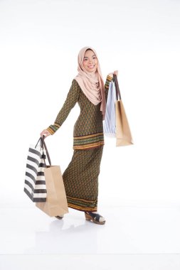 Geleneksel Asya elbisesi içinde güzel bir Müslüman bayan üniversite öğrencisi beyaz arka planda izole edilmiş alışveriş torbaları taşıyan modern kurung. Eidul Fitri moda ve festival alışveriş konsepti.