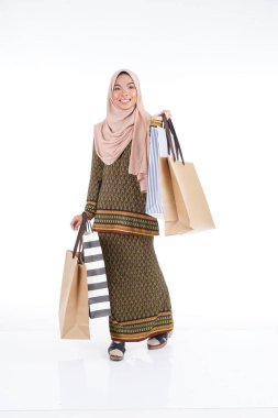Geleneksel Asya elbisesi içinde güzel bir Müslüman bayan üniversite öğrencisi beyaz arka planda izole edilmiş alışveriş torbaları taşıyan modern kurung. Eidul Fitri moda ve festival alışveriş konsepti.