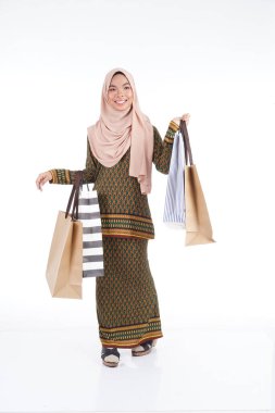 Geleneksel Asya elbisesi içinde güzel bir Müslüman bayan üniversite öğrencisi beyaz arka planda izole edilmiş alışveriş torbaları taşıyan modern kurung. Eidul Fitri moda ve festival alışveriş konsepti.