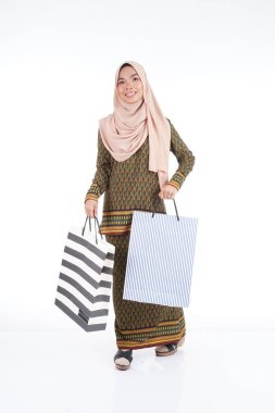 Geleneksel Asya elbisesi içinde güzel bir Müslüman bayan üniversite öğrencisi beyaz arka planda izole edilmiş alışveriş torbaları taşıyan modern kurung. Eidul Fitri moda ve festival alışveriş konsepti.