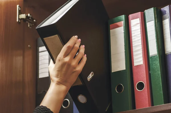 a woman officer pick a binder of document on the row of file fol