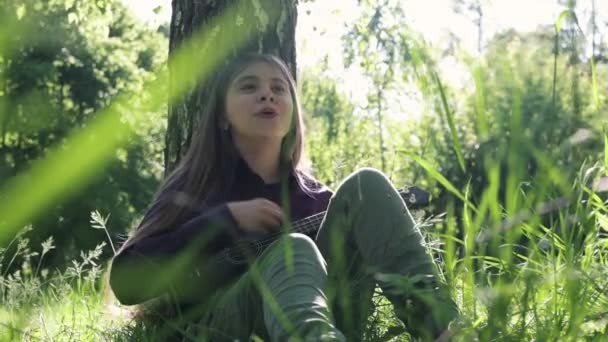 Teenager Mädchen Spielt Ukulele Park Einen Baum Gelehnt — Stockvideo