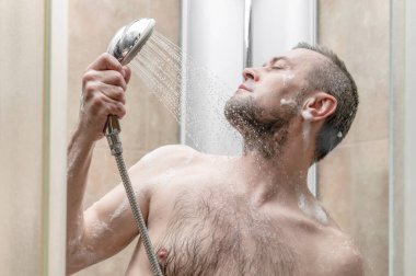 Adam modern fayanslı banyoda duş alıyor.