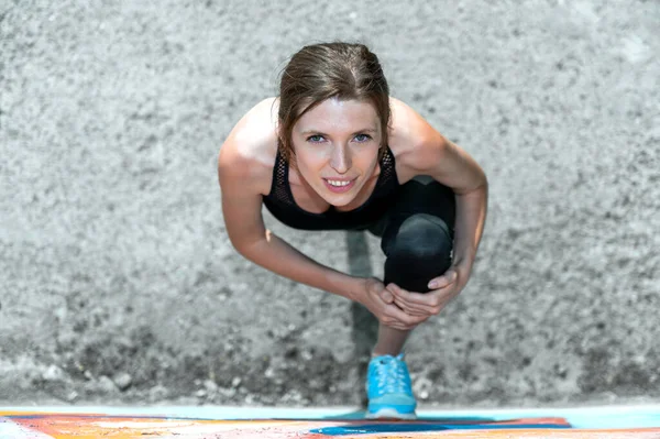 Young woman doing gymnastics on the street. Young woman doing sport exercise against colorful wall on city street. View from above