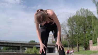 Genç bir kadın nehir kenarında koşup koştuktan sonra dinleniyor. Şehirdeki bir kardiyo egzersizinden sonra yorgun düşmüş güzel bir bayan sporcu. Koşu yaşam tarzı sağlıklı yaşam tarzı.