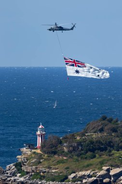 Sydney, Australia - October 4, 2013: Royal Australian Navy (RAN) Sikorsky S-70B-2 Seahawk Helicopter N24-001 flying the White Ensign of the RAN over Sydney Harbour.  clipart