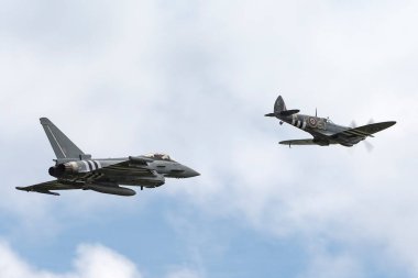 RAF Waddington, Lincolnshire, UK - July 6, 2014: Royal Air Force (RAF) Eurofighter EF-2000 Typhoon from No.29(R) Squadron flies in formation with a Supermarine Spitfire from the Battle of Britain Memorial Flight. clipart
