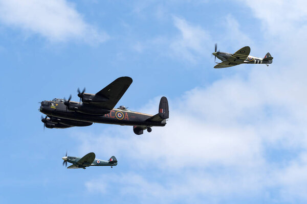 RAF Waddington, Lincolnshire, UK - July 5, 2014: Royal Air Force (RAF) Battle Of Britain Memorial Flight Avro Lancaster bomber PA474 flying in formation with two Supermarine Spitfire fighter aircraft.