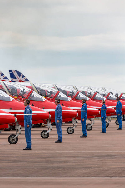 RAF Fairford, Gloucestershire, UK - July 12, 2014: Royal Air Force (RAF) Red Arrows ground crew members give directions to the pilots in their British Aerospace Hawk T.1 jet trainer aircraft as they start up in preparation for takeoff. 
