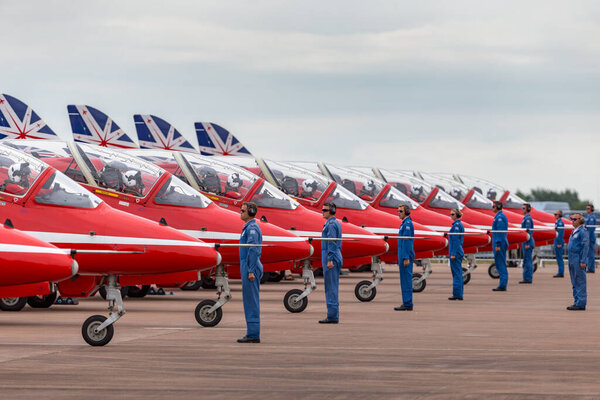 RAF Fairford, Gloucestershire, UK - July 12, 2014: Royal Air Force (RAF) Red Arrows ground crew members give directions to the pilots in their British Aerospace Hawk T.1 jet trainer aircraft as they start up in preparation for takeoff. 