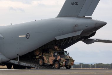 Avalon, Australia - February 27, 2015: Australian Army Bushmaster armoured Personnel carrier (APC) unloading from a Royal Australian Air Force Boeing C-17A Globemaster transport aircraft. clipart