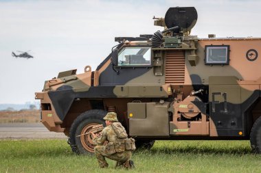 Avalon, Australia - February 27, 2015: Australian Army soldier with a Bushmaster armored personnel carrier (APC) and an Army Eurocopter Tiger helicopter. clipart