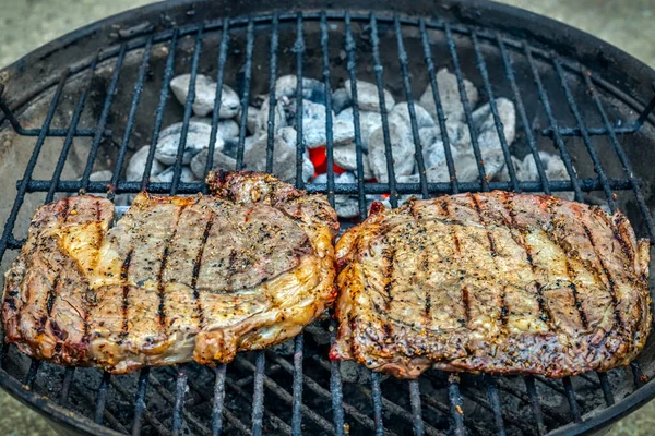 İki baharatlı biftek, küçük bir ızgarada kömürün üzerinde oturuyor..