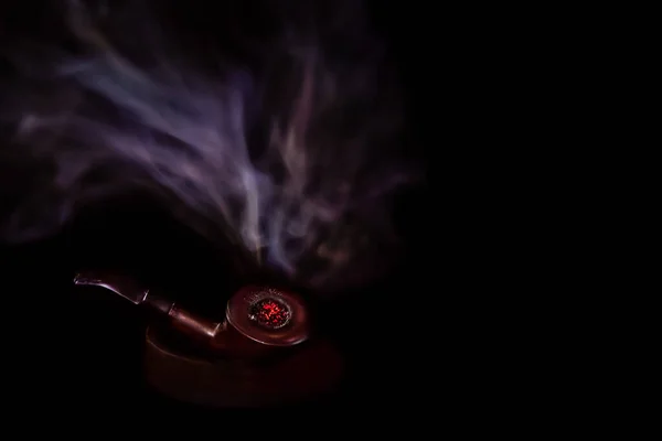 暗い部屋に座っている間に煙が上昇している赤い塊茎を持つ熱いパイプ — ストック写真