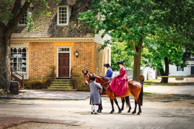Citizens of Colonial Williamsburg, in period clothing, meet in the street on horseback. clipart