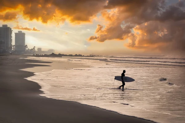 A surfer in a wet suit enters the water at the beach in Coronado, CA on a January morning.