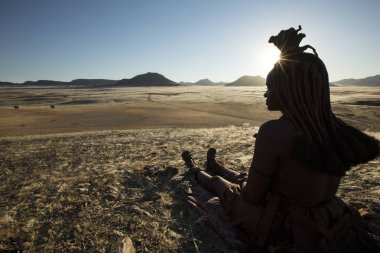 Orupembe, Kunene Region, Namibia. - May 13, 2018 : A young Himba woman herds her cattle home after a days grazing. The Himba still live a traditional nomadic life in the Kunene Region of Namibia clipart