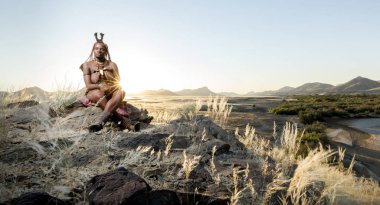 Orupembe, Kunene Region, Namibia. - May 13, 2018 : A young Himba woman herds her cattle home after a days grazing. The Himba still live a traditional nomadic life in the Kunene Region of Namibia clipart