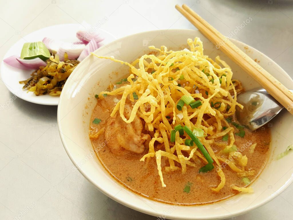 The name of Thai foods is khao soi, closeup view of curry noodles with coconut milk soup in a bowl with side dish is pickled vegetables on the table. 