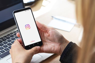 ROSARIO, ARGENTINA - 8 Mayıs 2020: Instagram ekranı olan kız. Elinde akıllı telefon ve sergilenen bir instagram logosu var. Genç iş kadını masasında, dizüstü bilgisayarının önünde..