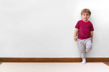 Serseri suratlı ve duvara yaslanmış bir çocuk. Beyaz arka plan. Evinde küçük bir çocuk. Boşluğu kopyala.