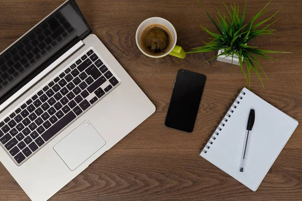 Top view of workspace. Table desk with laptop, cell phone, coffee, notepad, pen and plant with empty space background for design.