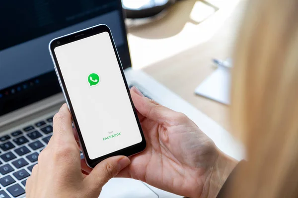 ROSARIO, ARGENTINA - 8 MAYIS 2020: başlat ekranı ile kız. Elinde akıllı telefon ve sergilenen bir Whatsapp logosuyla. İş yerindeki genç iş kadını, dizüstü bilgisayarın önünde..